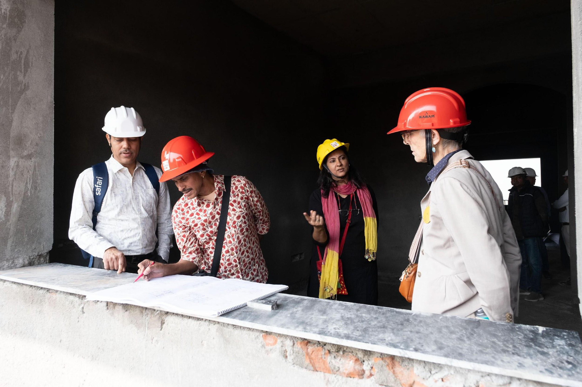 Architect and visitors in hard hats reviewing building plans on a concrete ledge during construction
