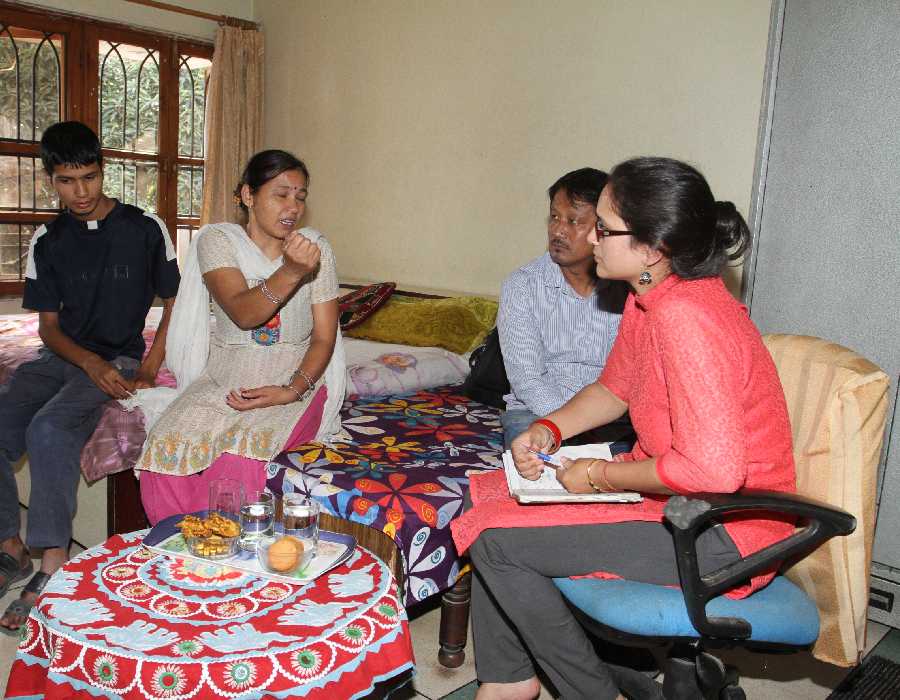 Counsellor with notebook speaking to a family seated on a bed during a home consultation