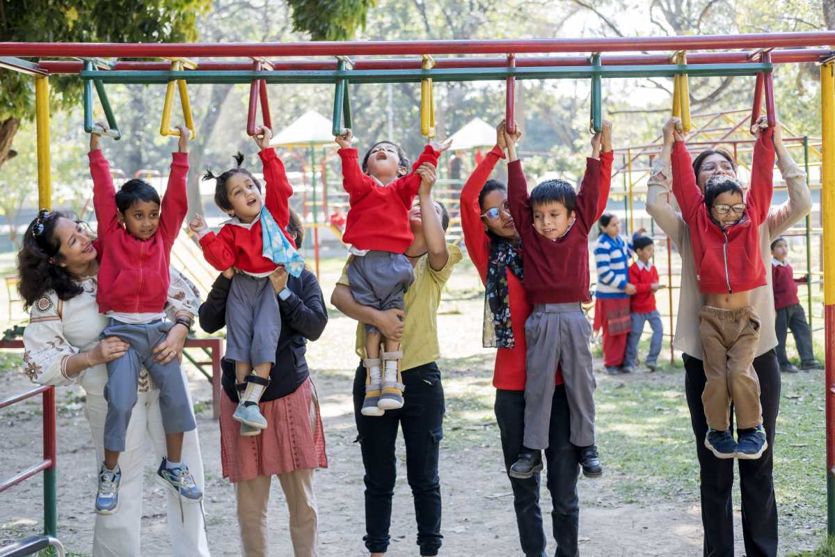 Therapists lifting children in red sweaters up to monkey bars on a playground