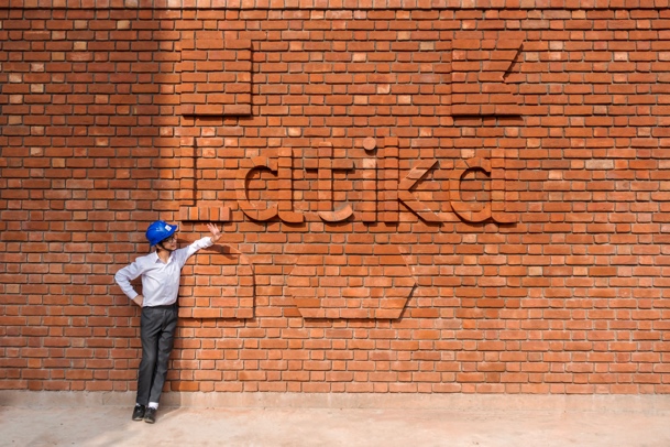 Construction worker in a blue hard hat beside a brick wall where the word “Latika” is inset into the brickwork itself