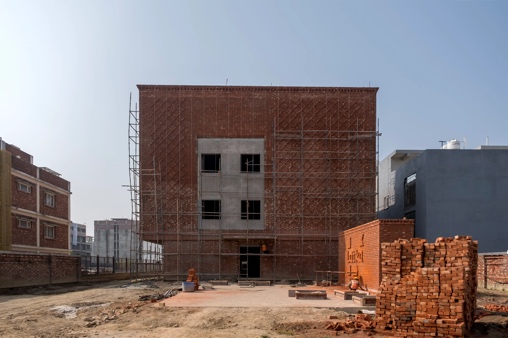 Mid-construction view of the new Latika building, scaffolding wrapping the brick exterior under a clear sky