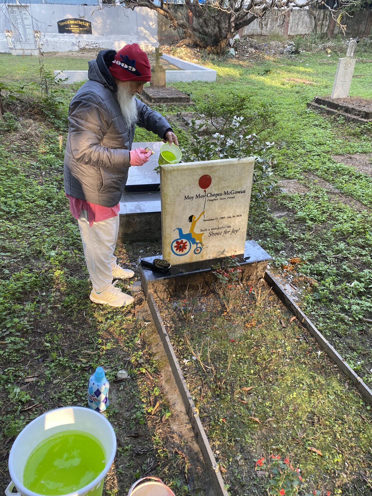 An older Latika friend in a red beanie tending Moy Moy Chopra-McGowan’s memorial in the garden