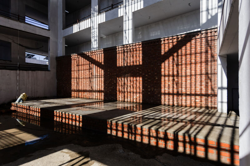 Striped sunlight pattern from a perforated screen falling across the brick wall and concrete platform of the new Latika building