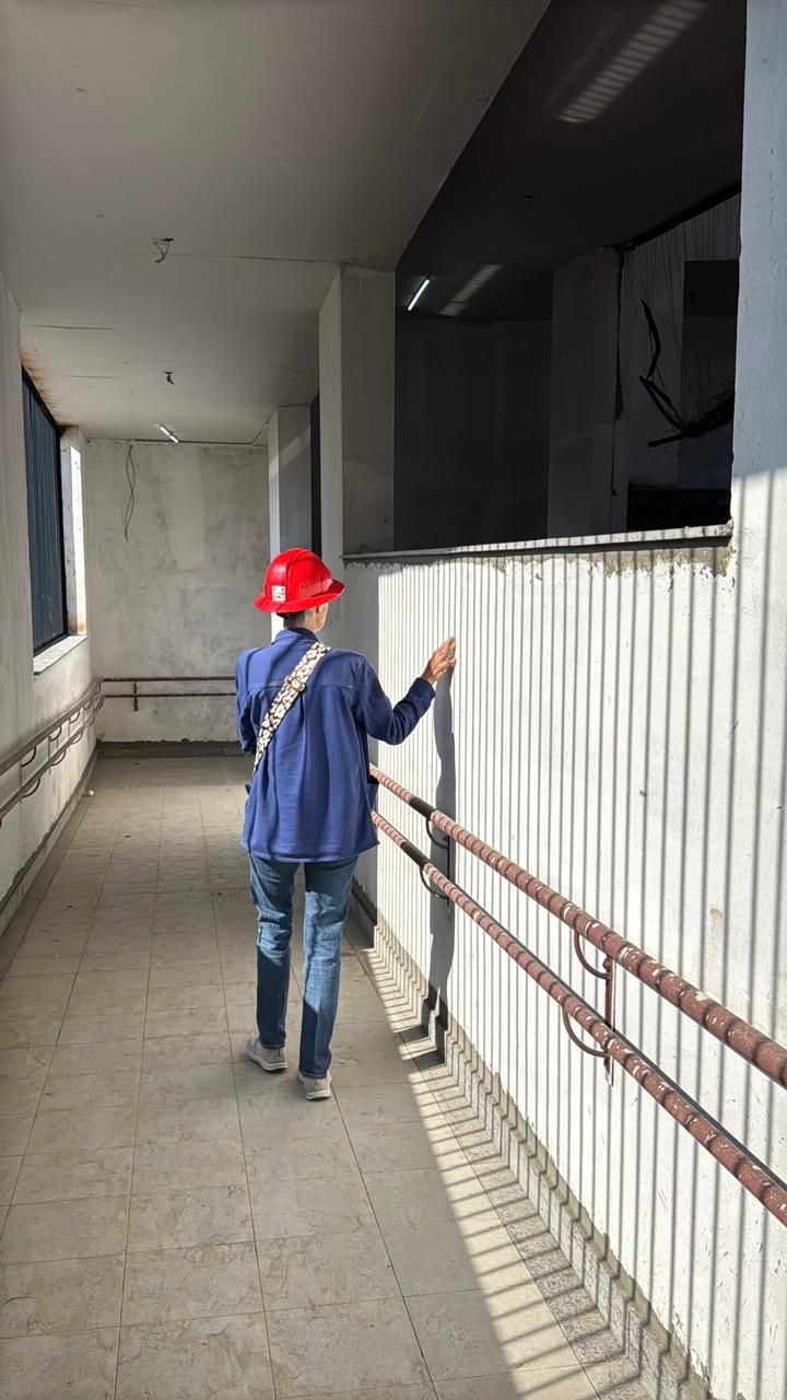 A person in a red hard hat walks a corridor of the new building, hand brushing the perforated screen as sunlight stripes the floor