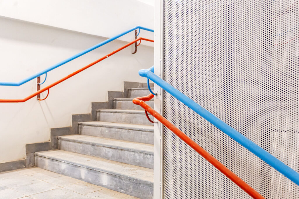 Bright blue and orange handrails along a clean concrete staircase in the new Latika building