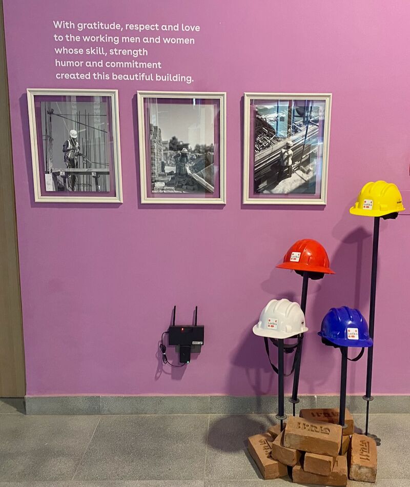 Tribute wall for the construction workers — three framed black-and-white photographs, four coloured hardhats on stands, and a thank-you message