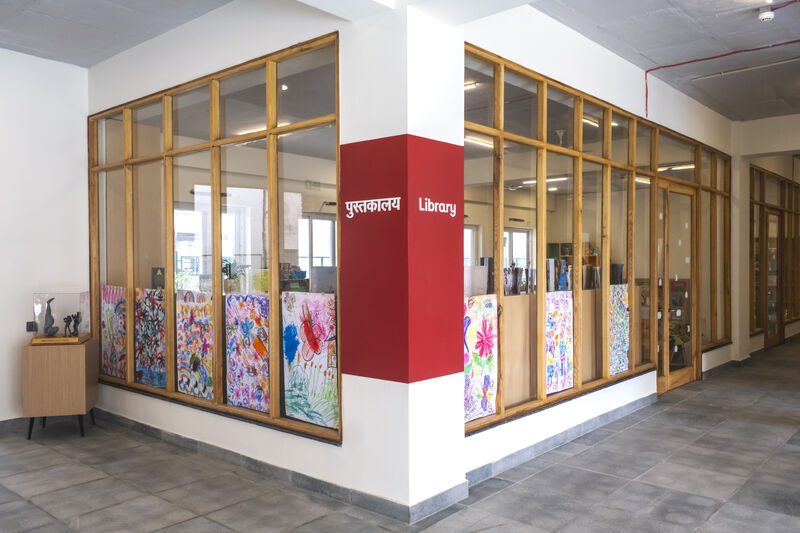 Exterior view of the new Latika library through its tall wooden-framed windows, children’s artwork displayed inside