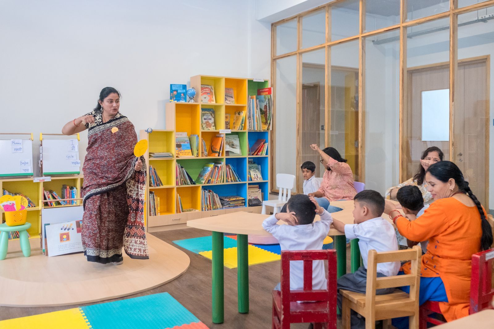 A Latika teacher in a sari leading storytime with a small group of children at the colourful library tables