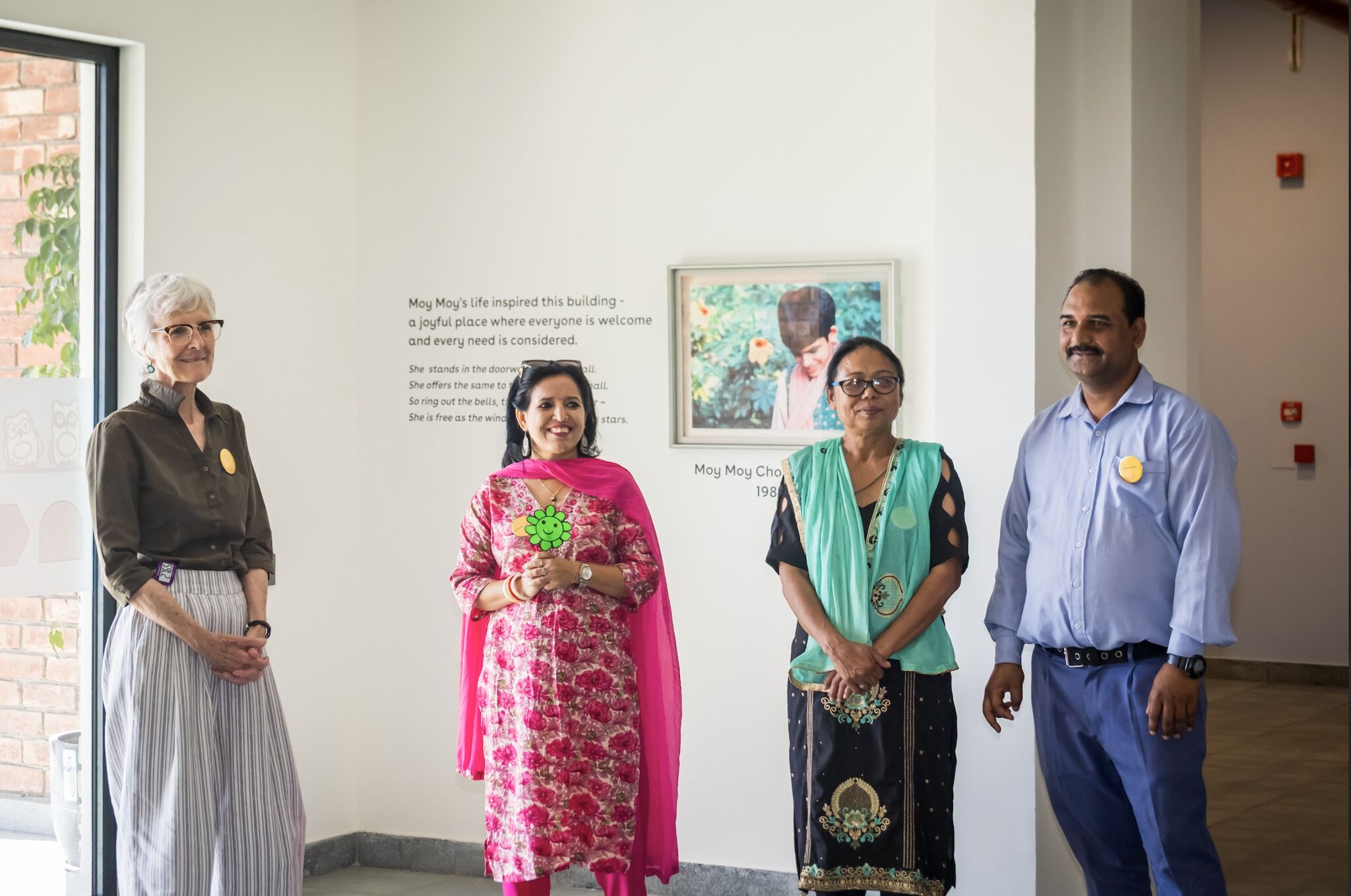 Four Latika team members pose in front of the Moy Moy Chopra-McGowan memorial wall on opening day
