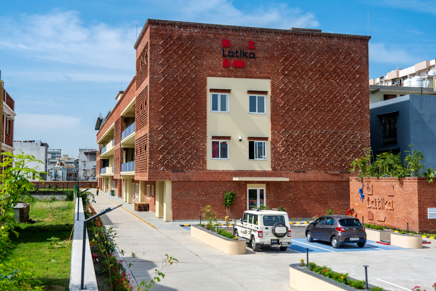 Side view of a brick Latika building with red lettering, cars in the lot, and a garden alongside