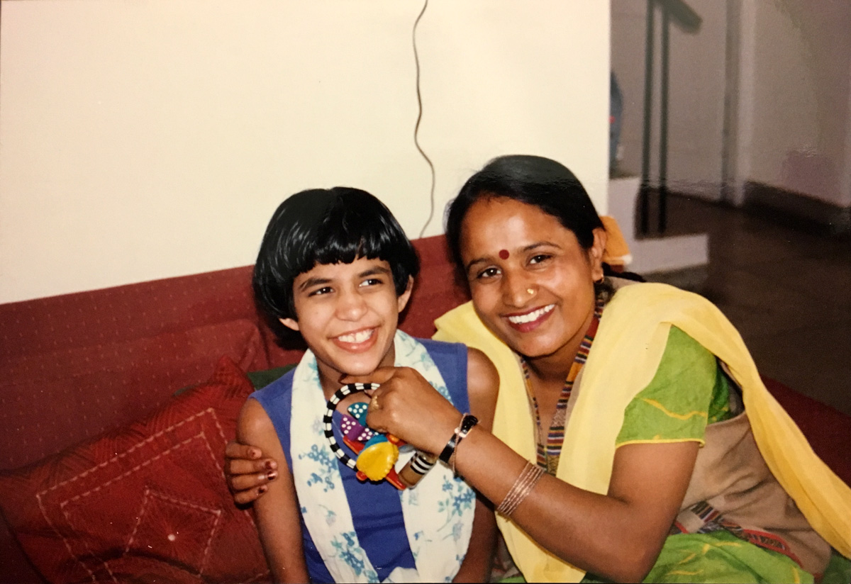 Smiling Moy Moy with bobbed hair seated with a woman in a green sari holding a colourful toy