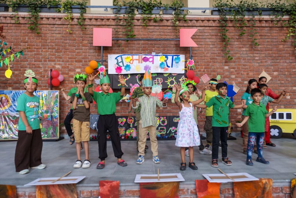 Children in green outfits and leafy crowns perform the finale Ek Chidiya, Anek Chidiyan with hands raised on the Samavesh stage