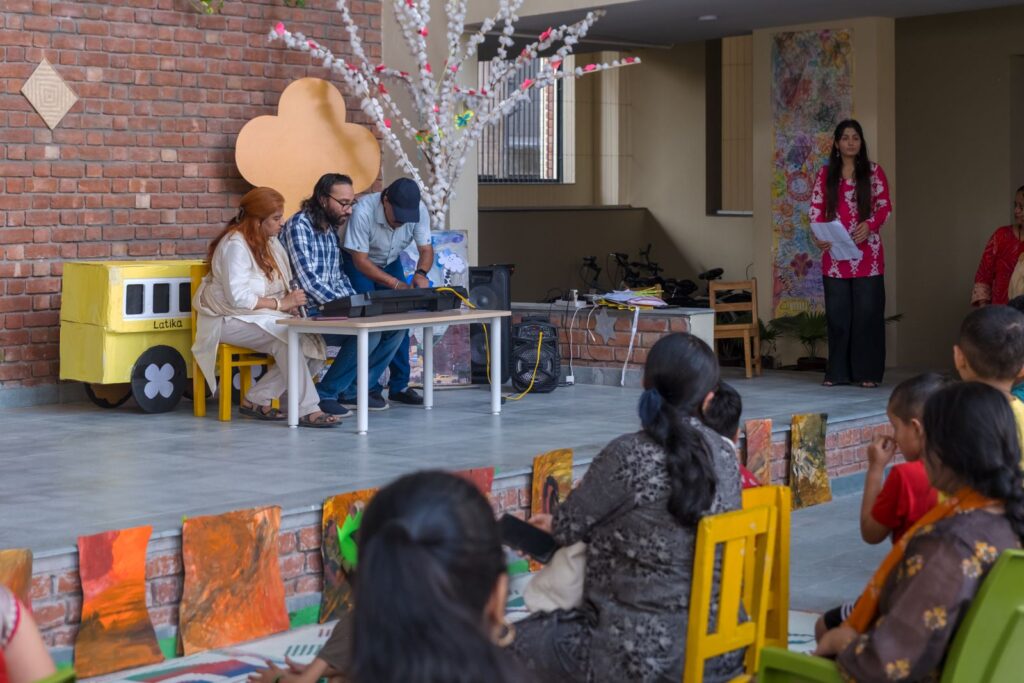 Two young performers at a keyboard with a microphone on the Samavesh stage as staff help set up and the audience watches