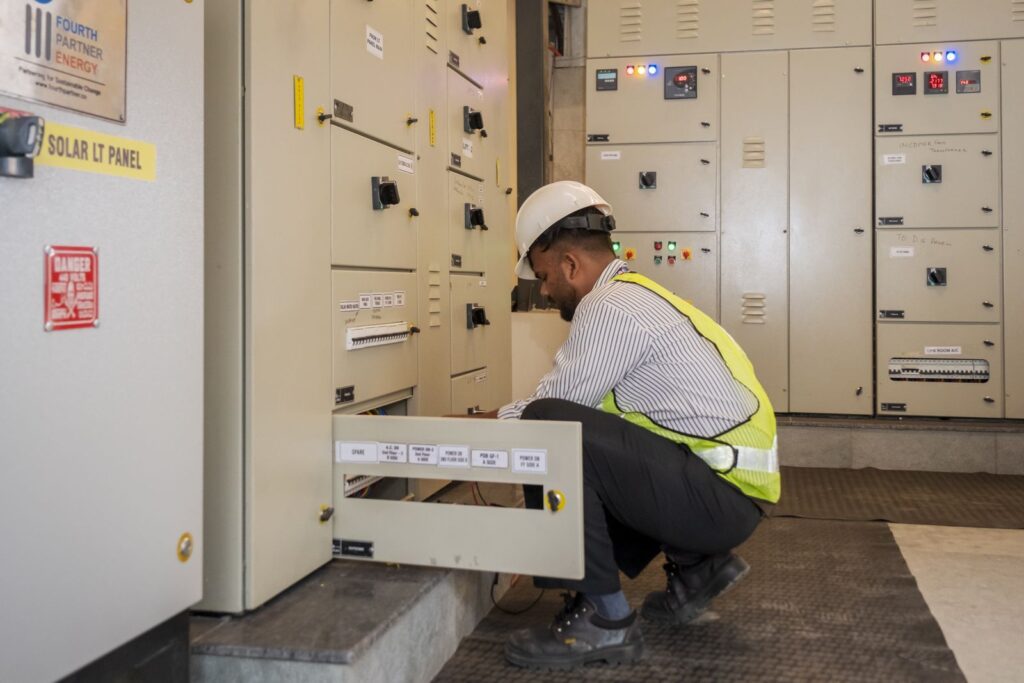 A technician in a hard hat and hi-vis vest working on the building's main electrical distribution panels