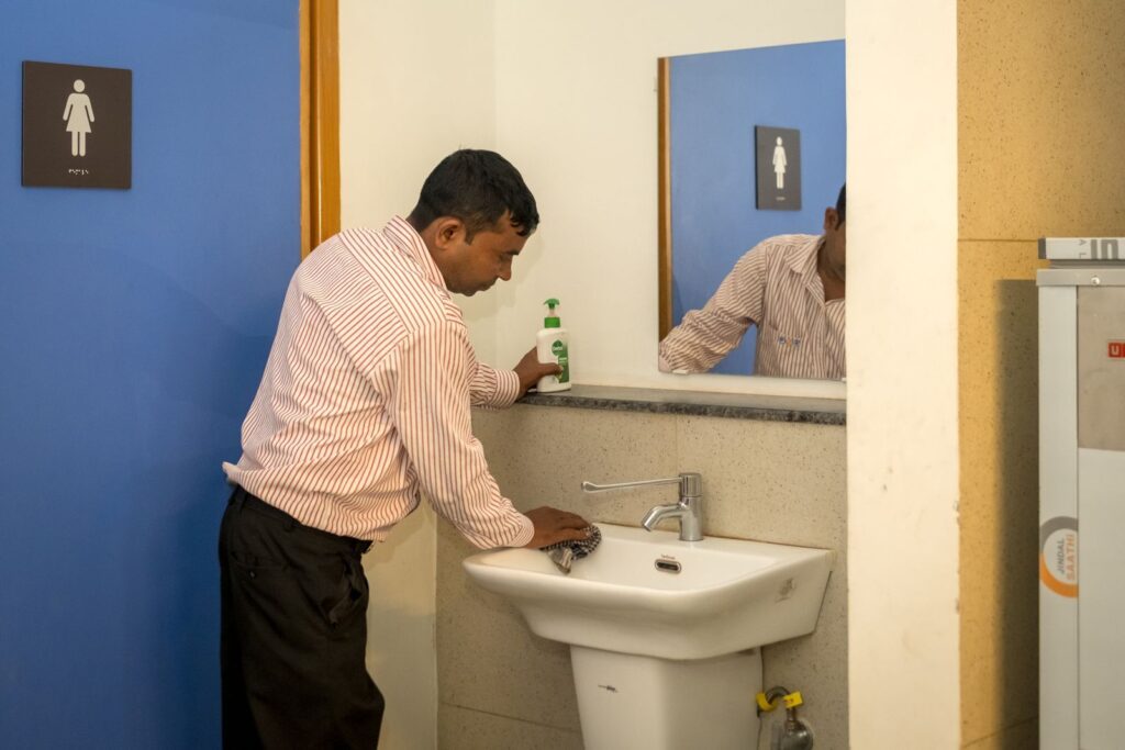 A staff member wiping down a washbasin in a clean restroom