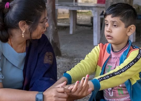 A therapist works one-on-one with a boy at an outdoor table at Latika